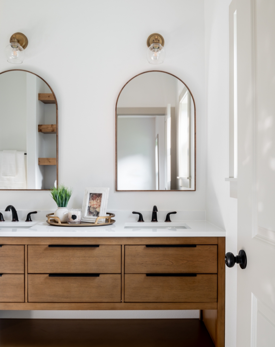 A bathroom with two sinks and two arched mirrors.