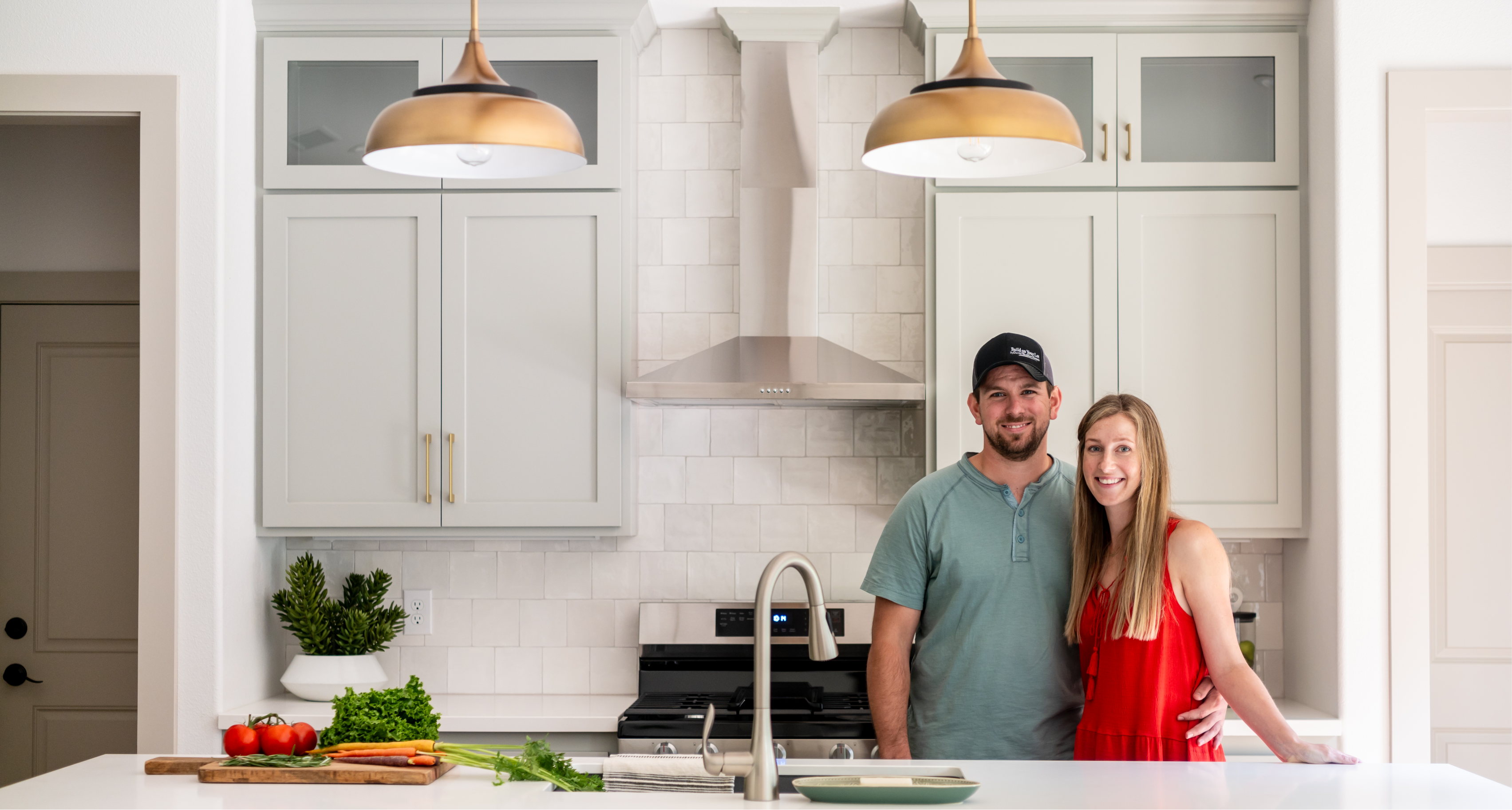 A man and a woman standing and smiling in a kitchen.