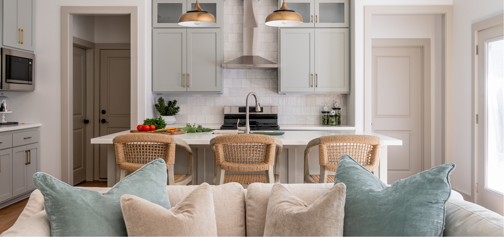 A couch with pillows in front of a kitchen with chairs.