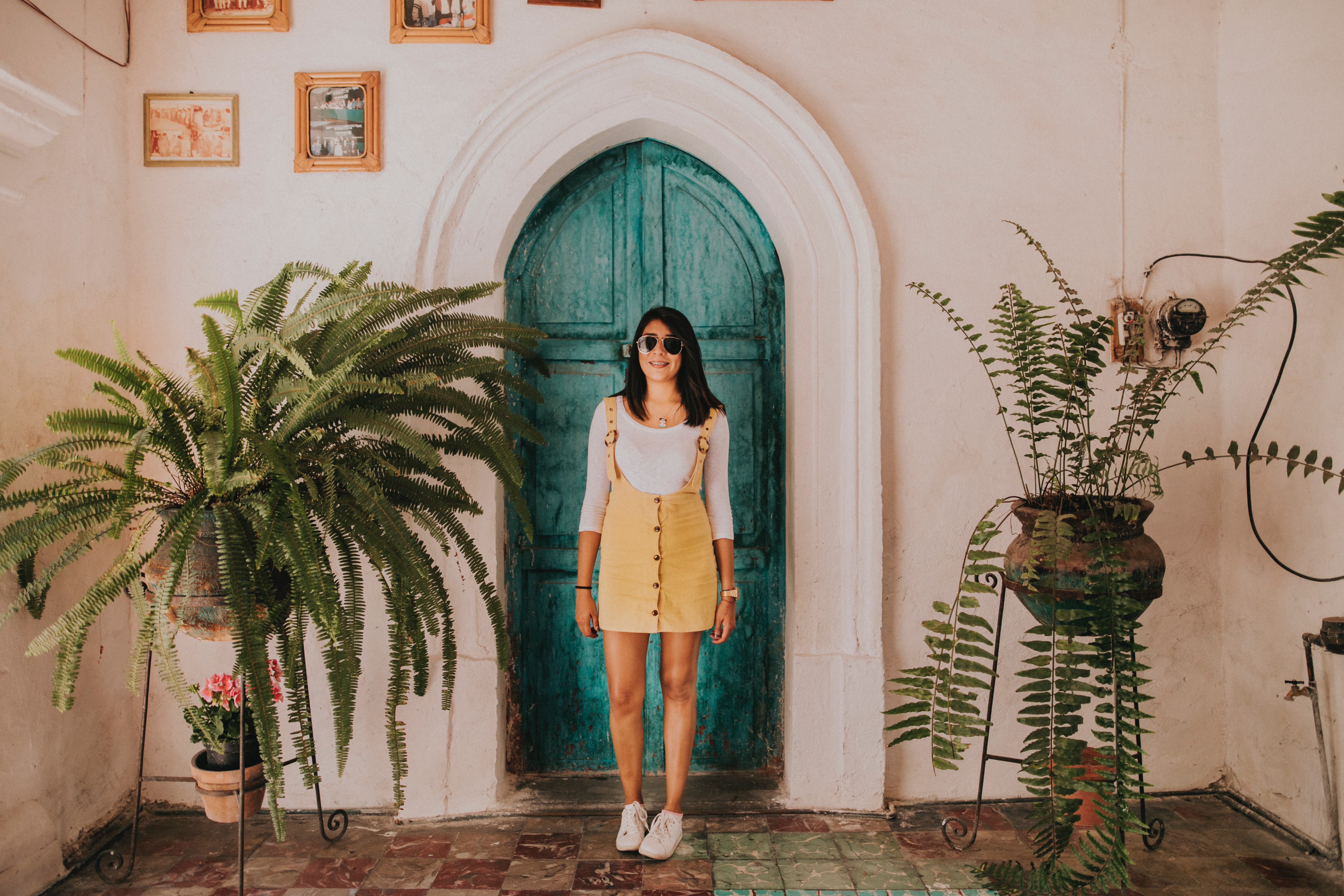 A woman standing in front of an aqua, arched doorway next to plants. 