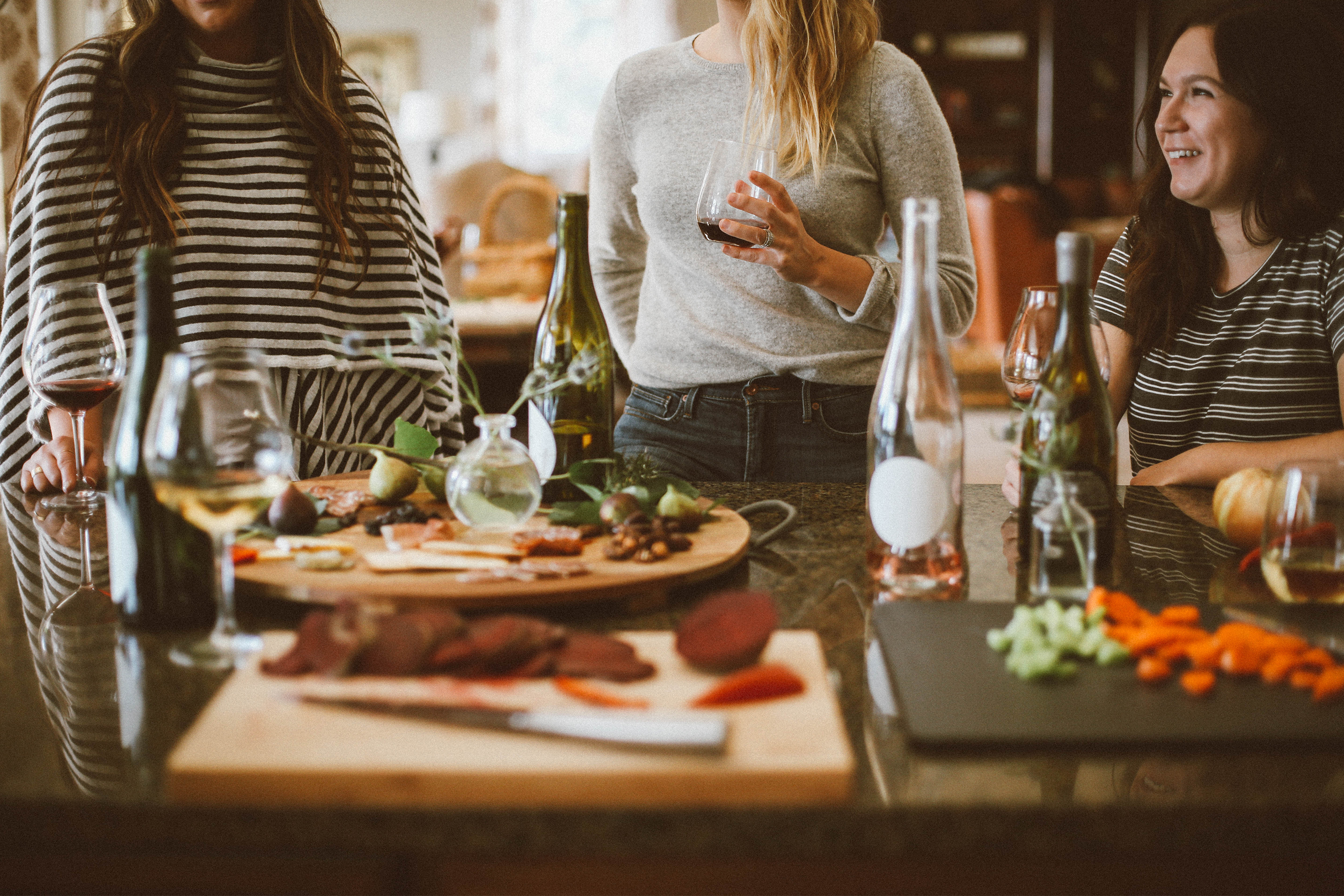 A group of three women drinking wine and eating food.