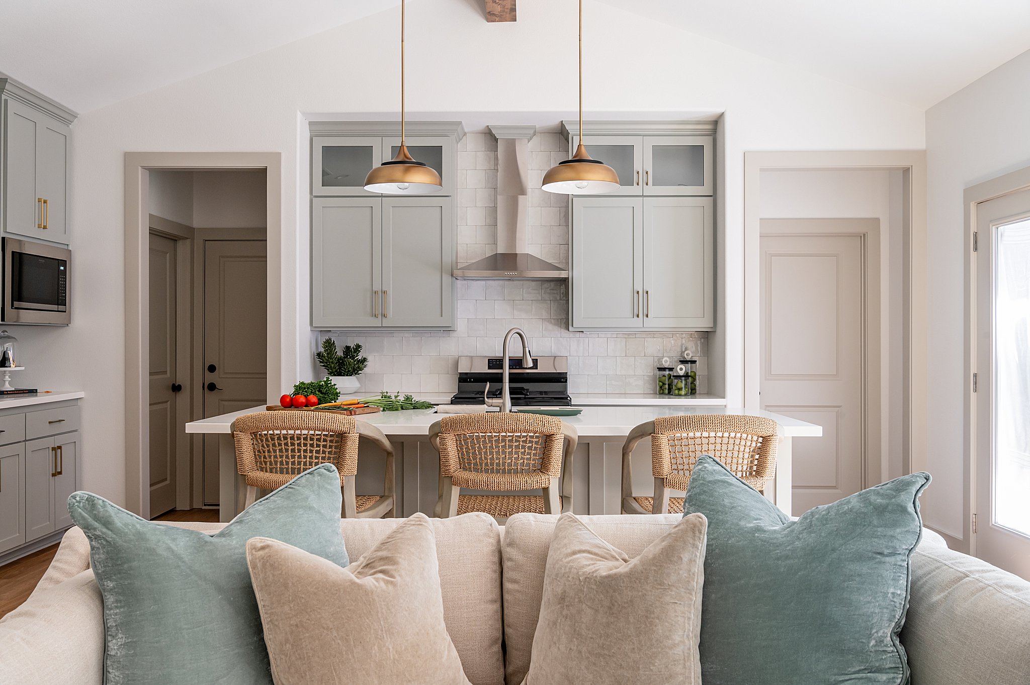 A couch with pillows in front of a kitchen with chairs.