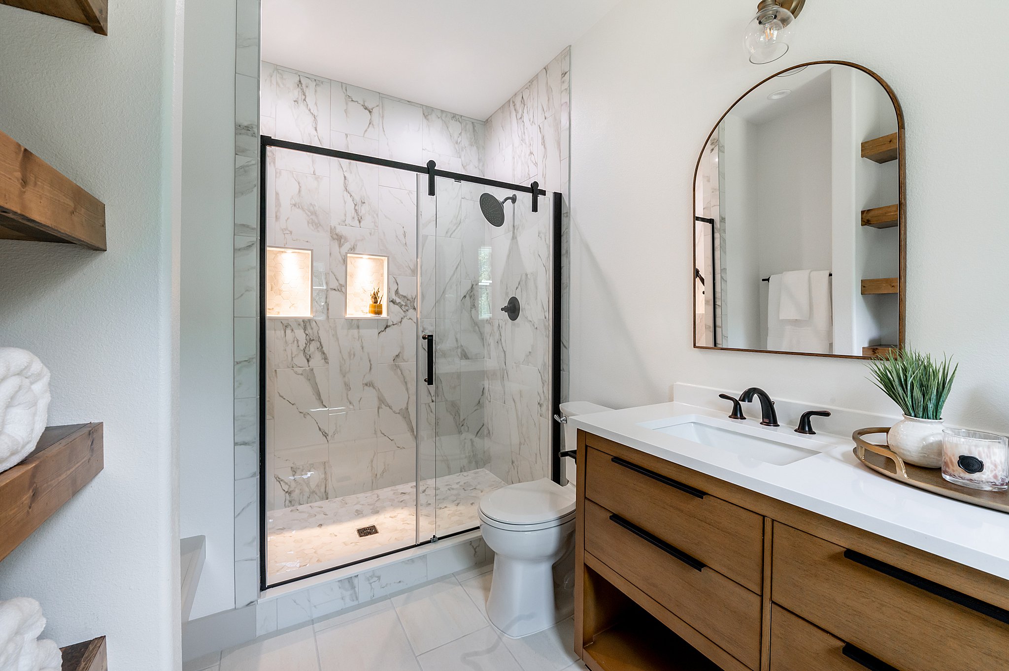 A glass shower and a sink with an arched mirror.