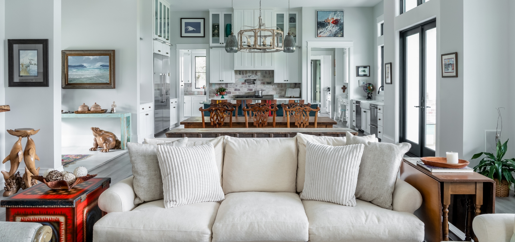 A couch with pillows in front of a kitchen with chairs.